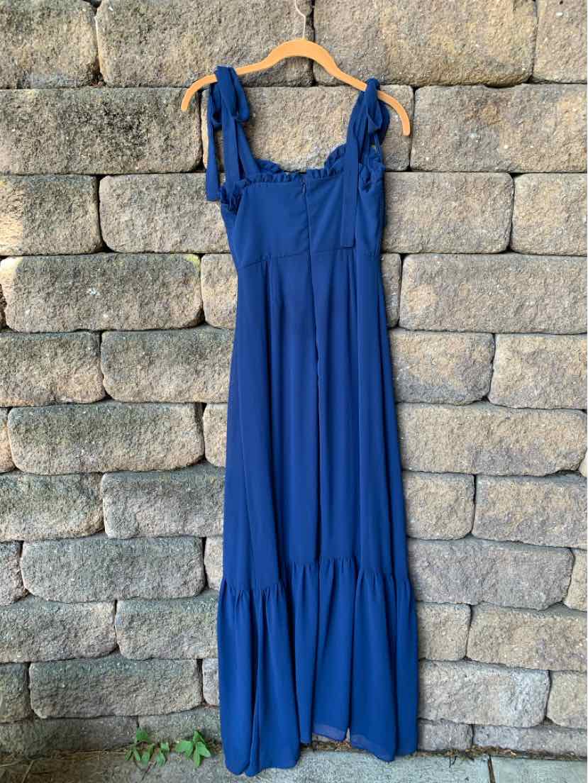 Royal blue sleeveless maxi dress with tie shoulder straps and tiered hem hanging on wooden hanger.