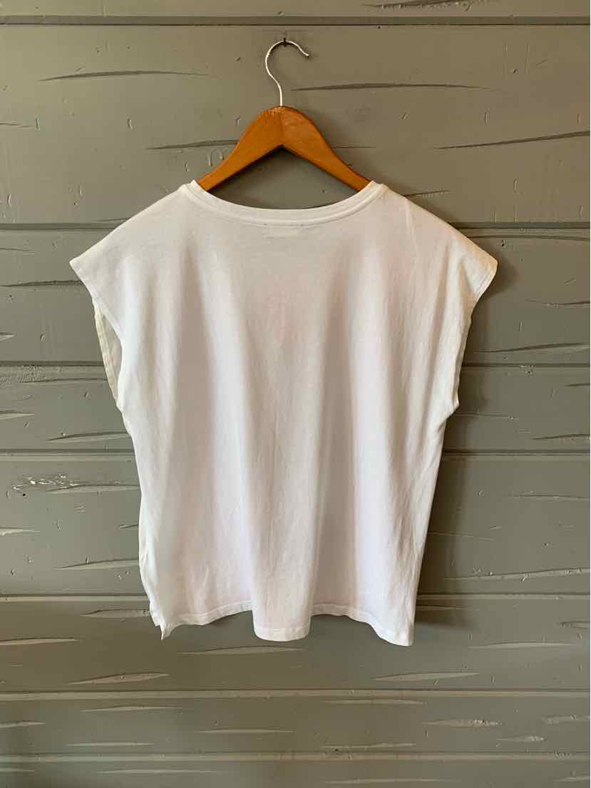 White sleeveless top with wide shoulder cut and loose fit, hanging on wooden hanger against gray wooden wall.