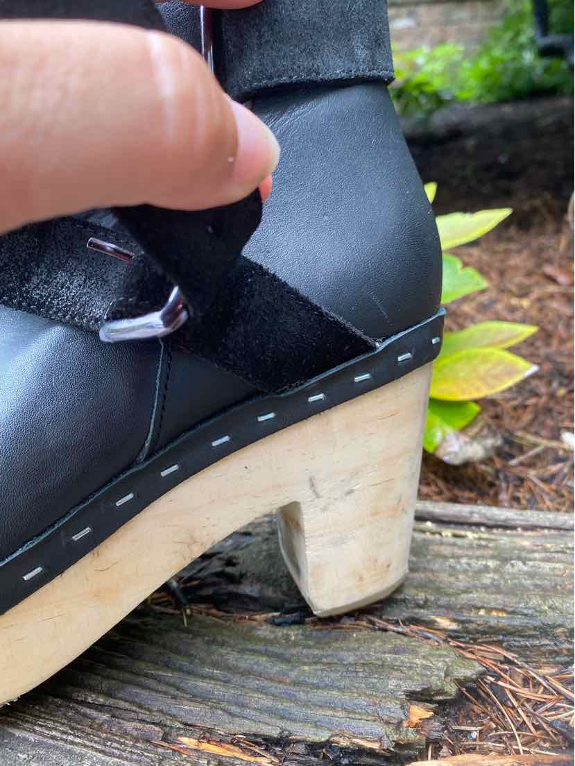 Black leather ankle boot with suede strap detail, light wooden block heel, and stitched sole.