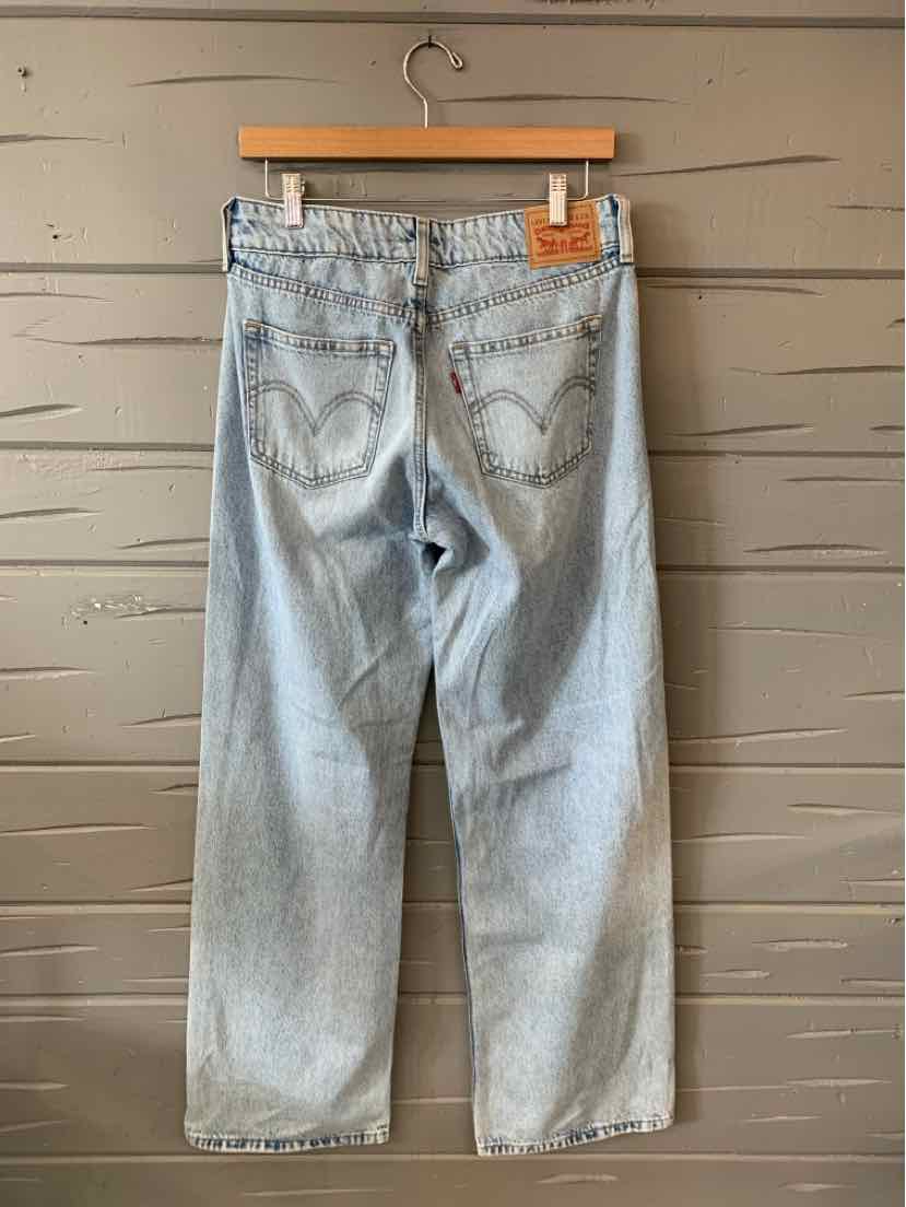 Light blue high-waisted Levi’s denim jeans with straight legs and classic back pockets hanging on wooden hanger against gray