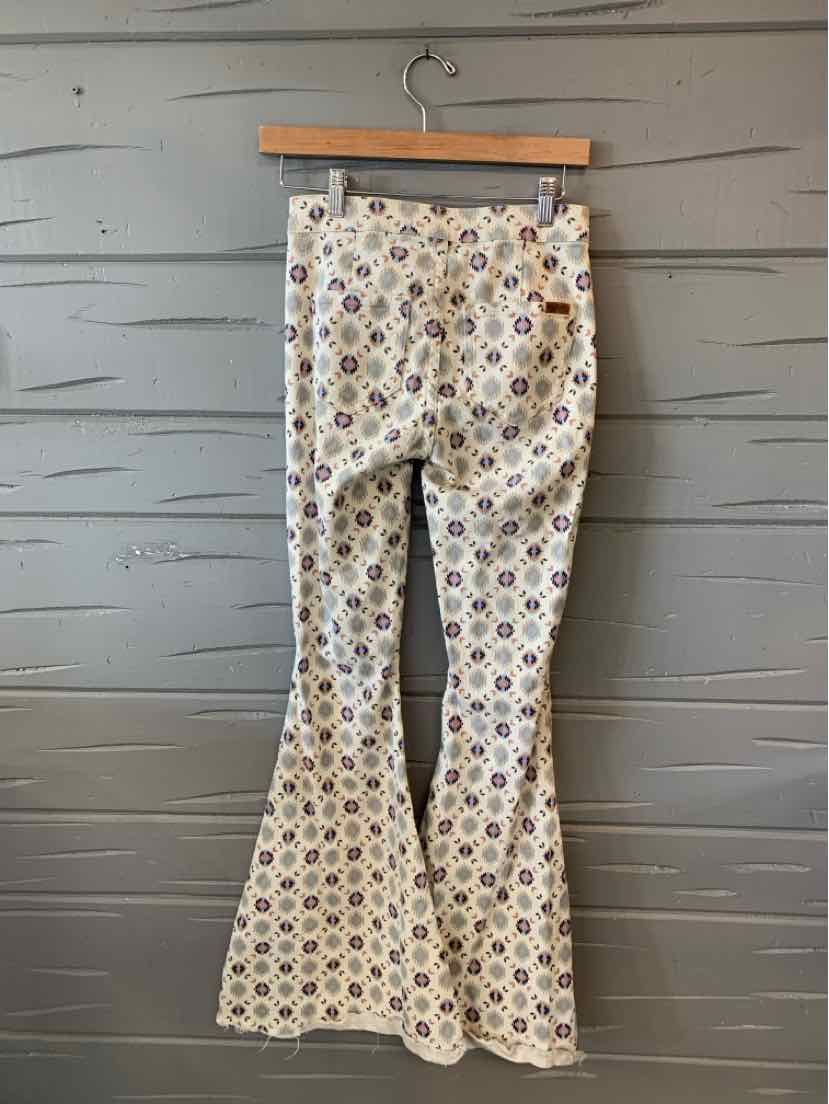 High-waisted beige pants with a colorful geometric pattern and flared legs hanging on a wooden hanger.