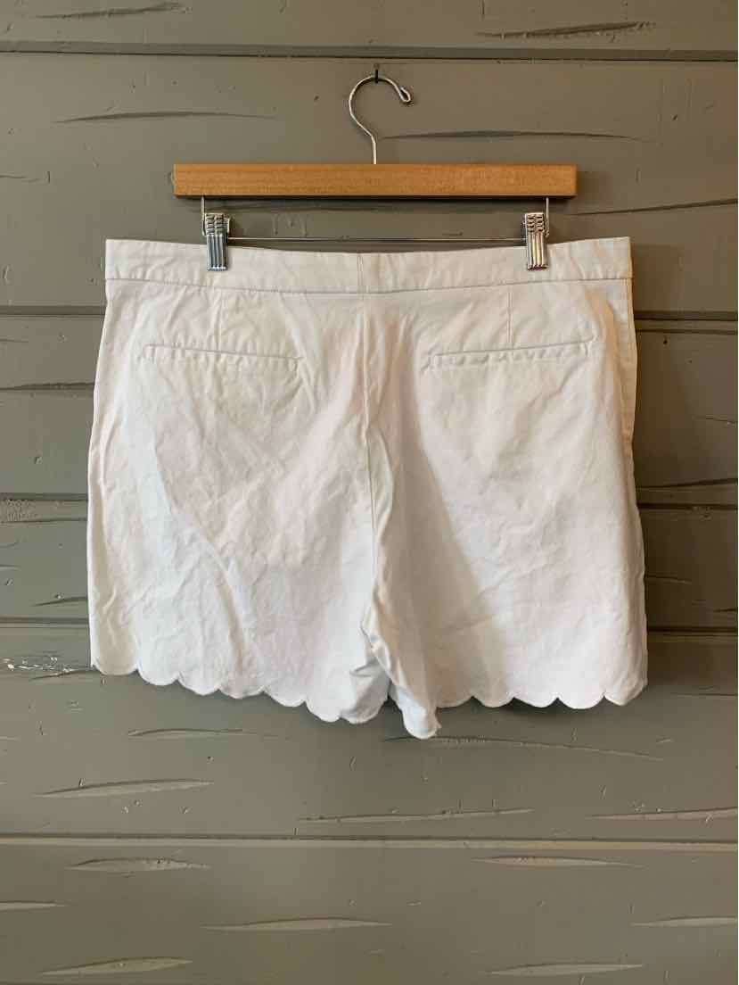 White cotton shorts with scalloped hem and back welt pockets, size 14, hung on wooden hanger.
