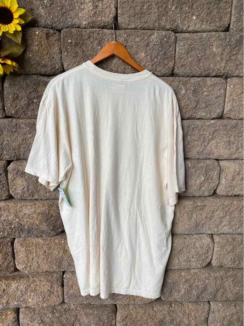 Plain white oversized short-sleeve T-shirt in XXL, hanging on wooden hanger against stone wall.