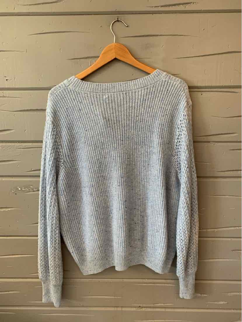 Light gray knitted sweater with long sleeves, ribbed neckline, cuffs, and hem, hanging on wooden hanger.