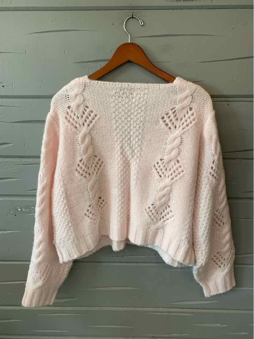 Pale pink cropped knit sweater with a crew neckline, balloon sleeves, and openwork diamond patterns, hanging on a wooden.