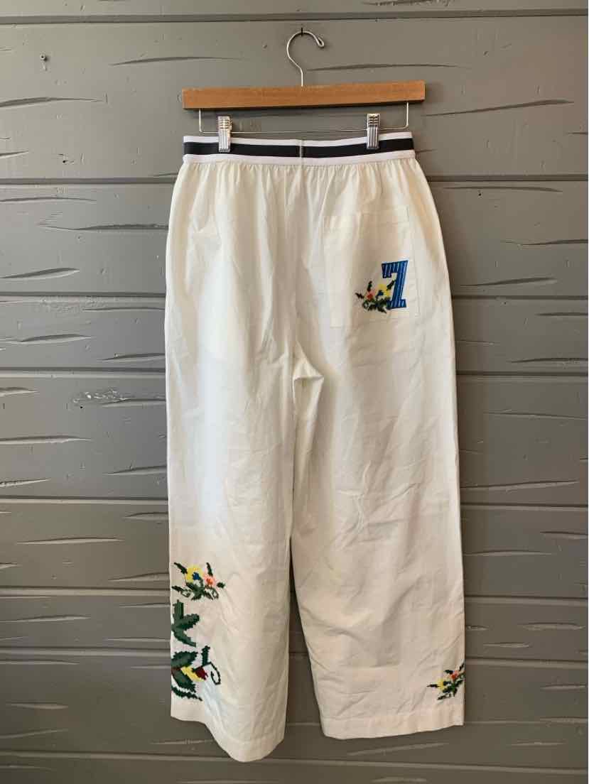 Cream wide-leg pants with colorful floral embroidery near the right hip and left ankle, elastic waistband.