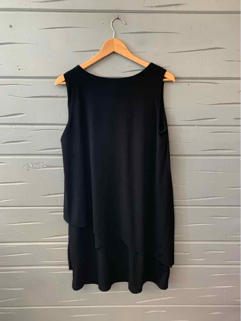 Sleeveless black solid dress with scoop neckline hanging on wooden hanger against gray wooden wall.