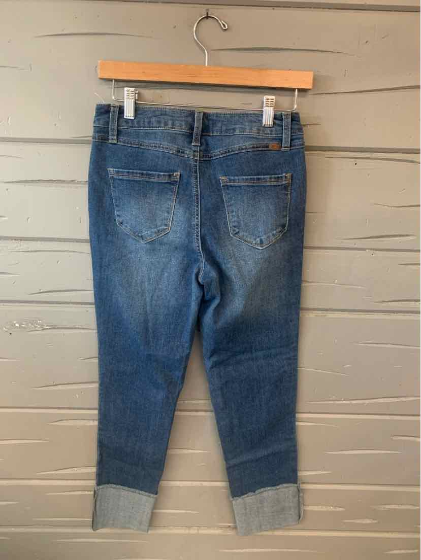Blue denim jeans with cuffed hems and back pockets hanging on wooden hanger.