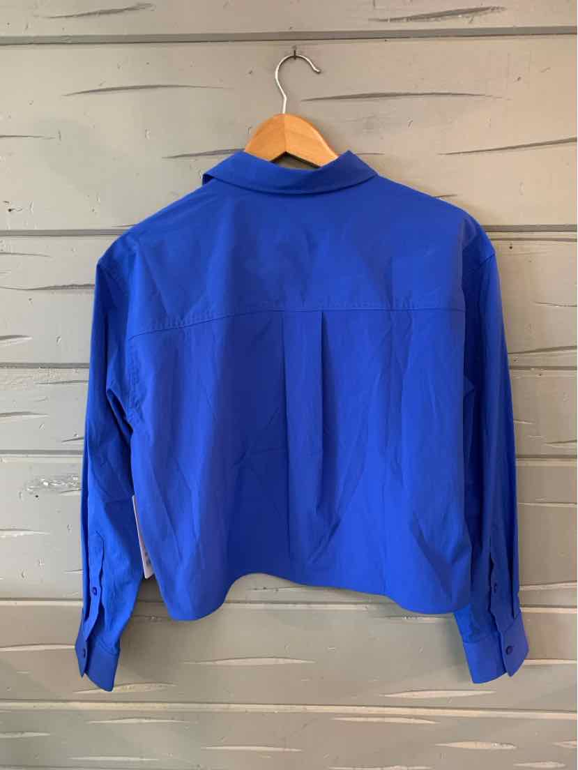 Cropped royal blue long-sleeve shirt with buttoned cuffs and pointed collar hanging on wooden hanger.
