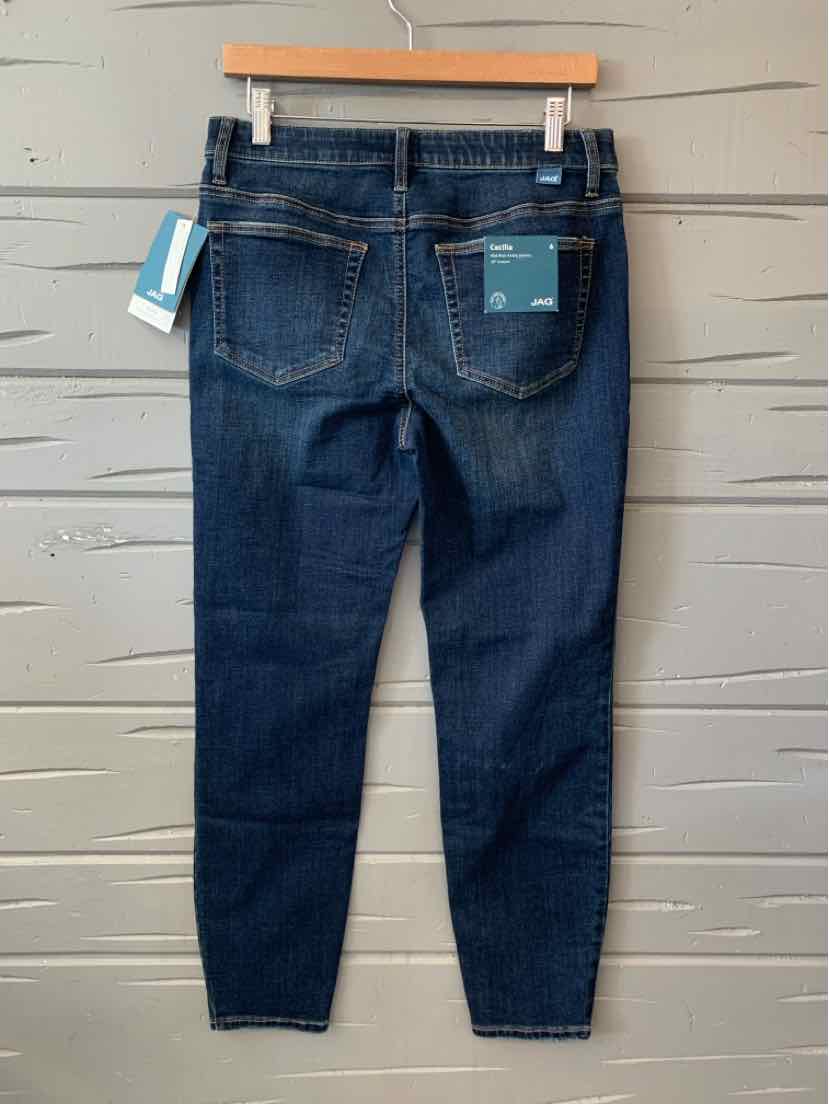 Dark blue denim slim-fit jeans with back pockets hanging on wooden hanger against gray wall.