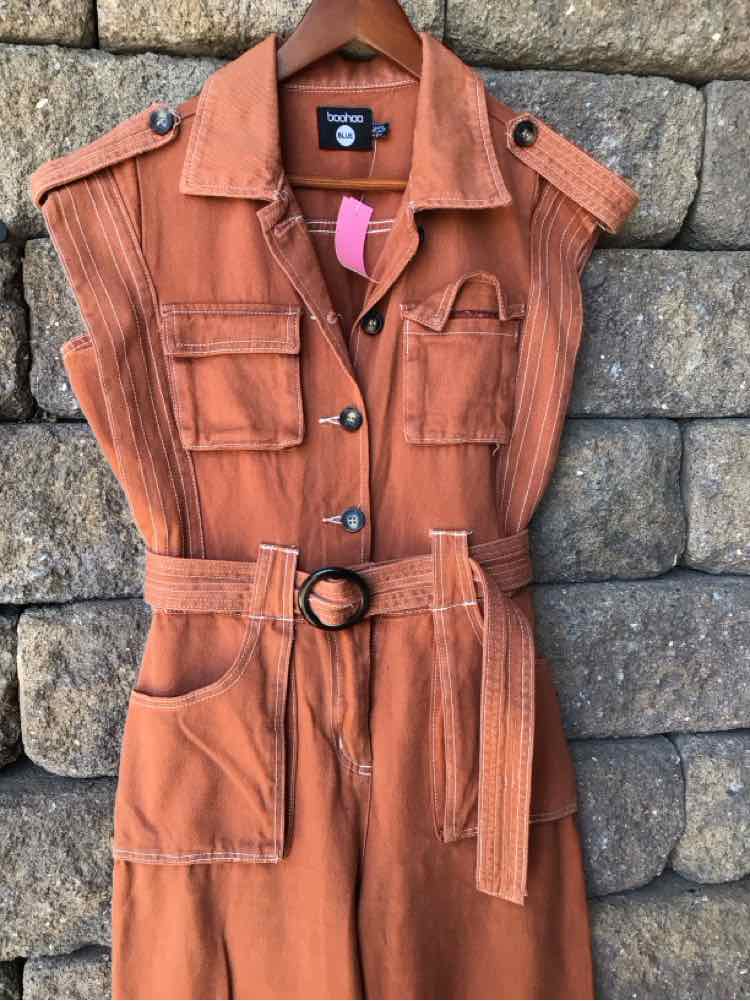 Rust-orange sleeveless denim jacket dress with front pockets, black buttons, epaulettes, and matching belt with ring buckle.