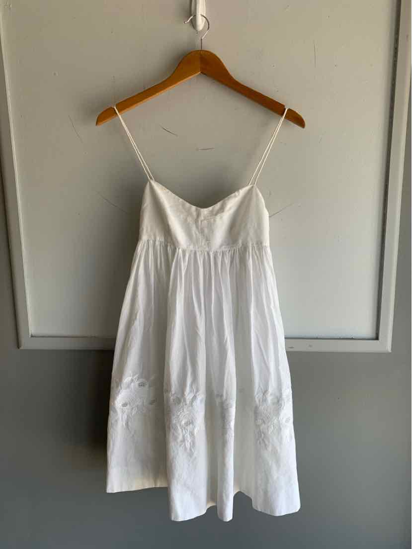 White sleeveless cotton dress with thin spaghetti straps and a gathered waist hanging on wooden hanger.