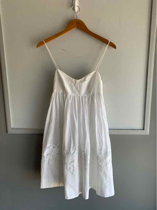 White sleeveless cotton dress with thin spaghetti straps and a gathered waist hanging on wooden hanger.