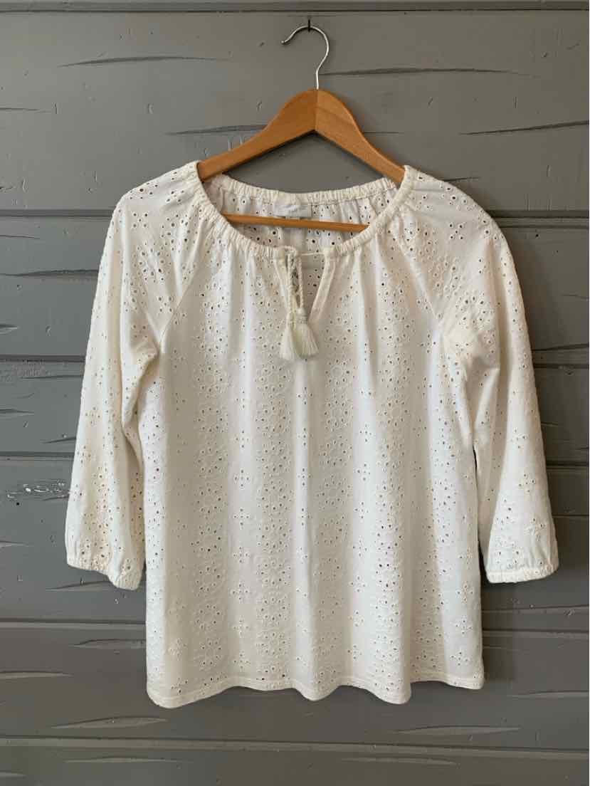 White eyelet blouse with three-quarter sleeves and a tie neckline hanging on wooden hanger.
