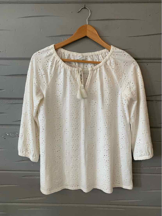 White eyelet blouse with three-quarter sleeves and a tie neckline hanging on wooden hanger.