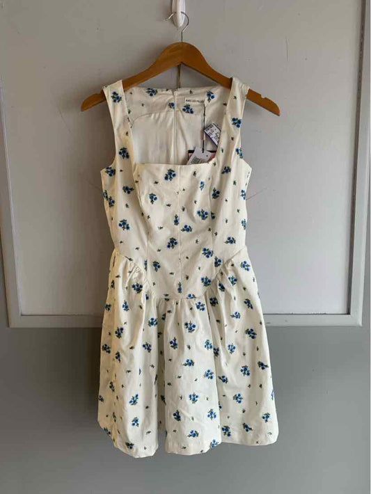 White sleeveless dress with blue floral print and square neckline on wooden hanger.