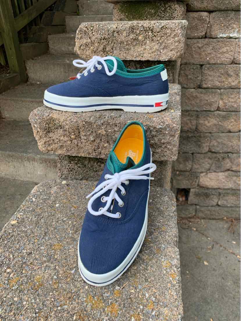 Navy blue low-top sneakers with white laces, white rubber sole, and teal collar trim.