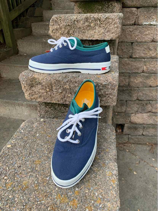 Navy blue low-top sneakers with white laces, white rubber sole, and teal collar trim.