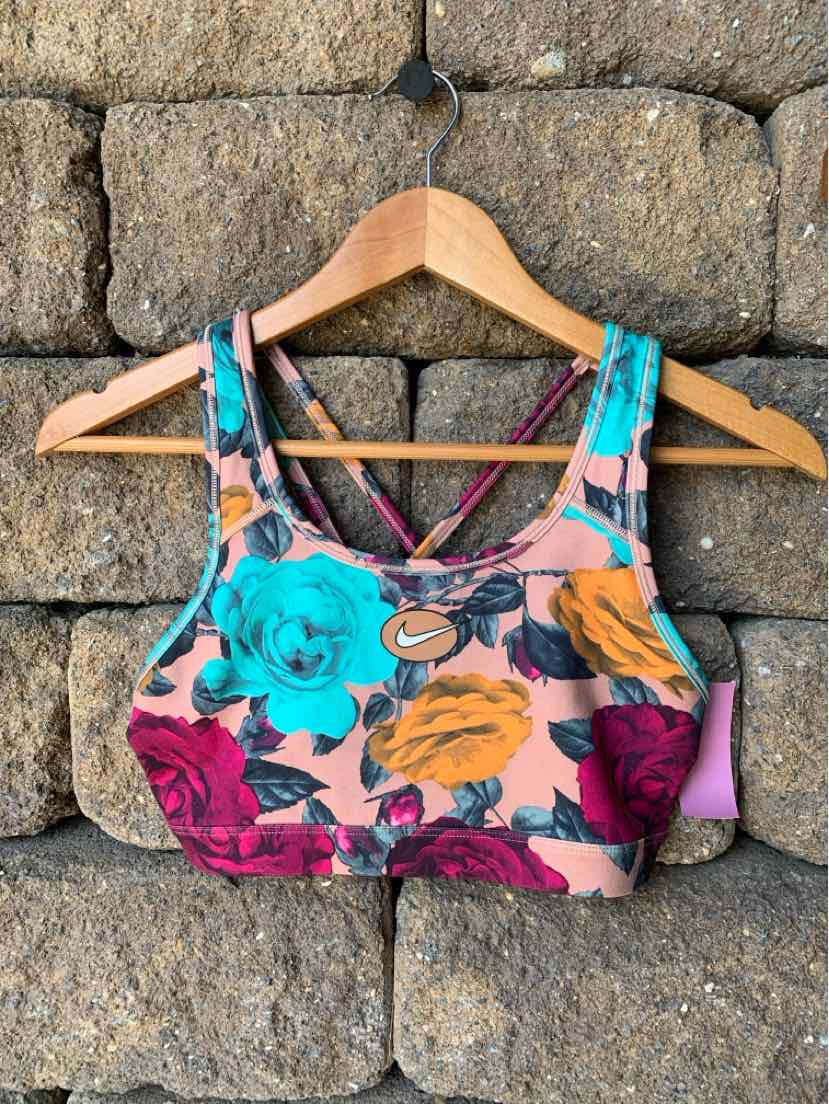 Women's Nike sports bra with vibrant floral print in teal, orange, and maroon on pink background.