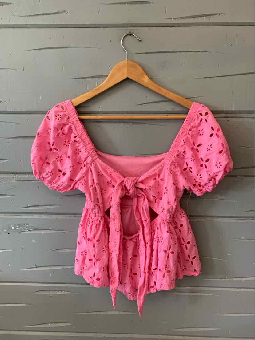 Pink eyelet lace blouse with puff sleeves and front tie waist on wooden hanger.