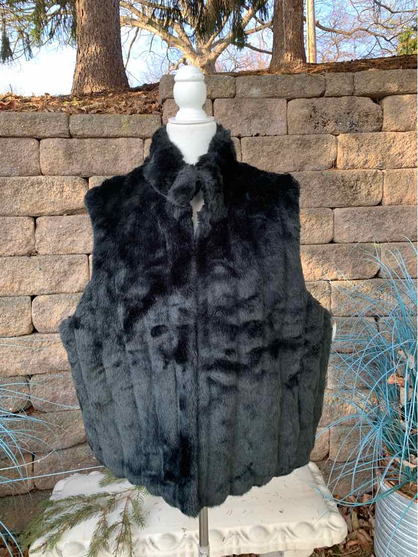 Black faux fur sleeveless vest with high collar, size L/XL on white mannequin against stone wall background.