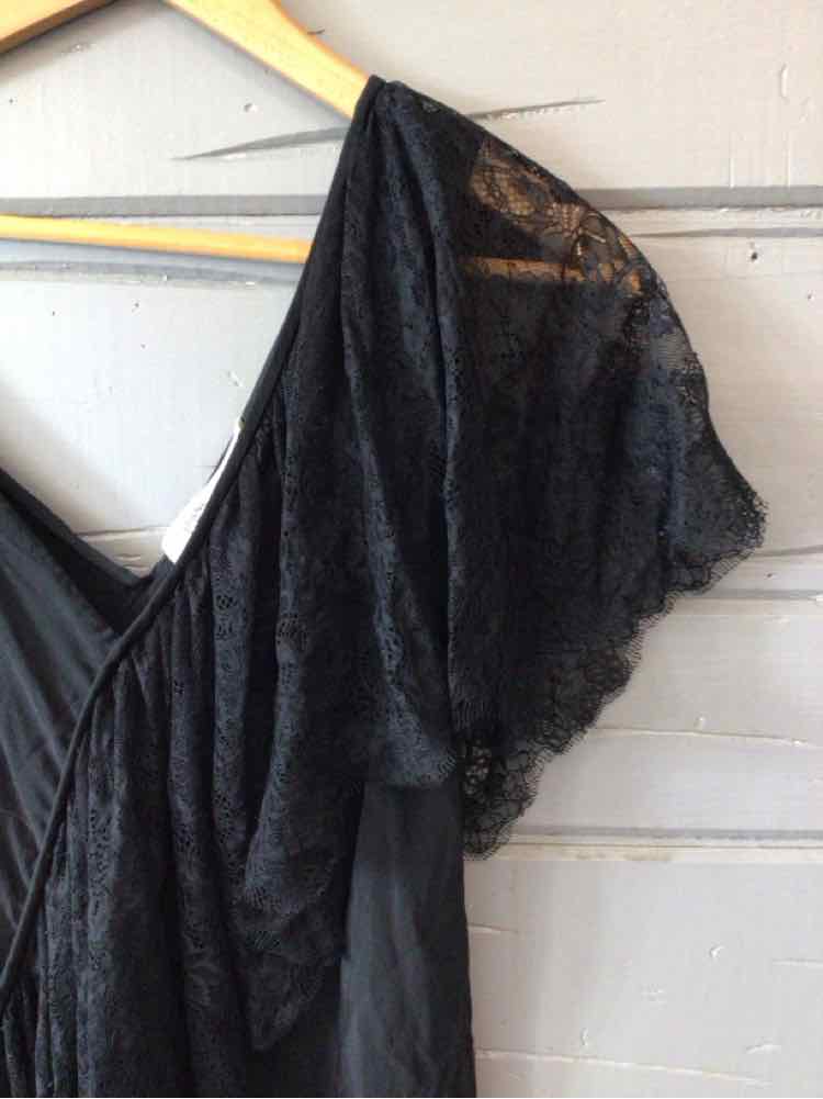 Black lace short sleeve blouse with scalloped edges hanging on wooden hanger.