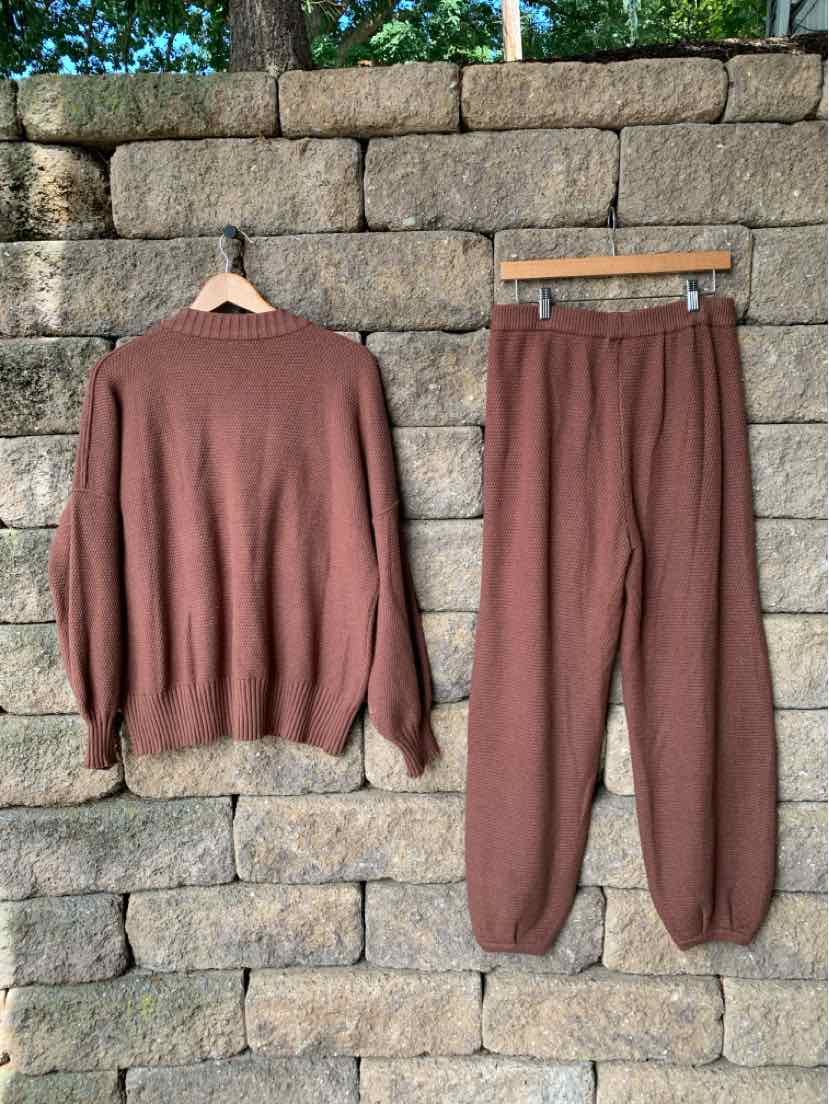 Brown knit long-sleeve sweater and matching knit jogger pants set hanging against stone wall.
