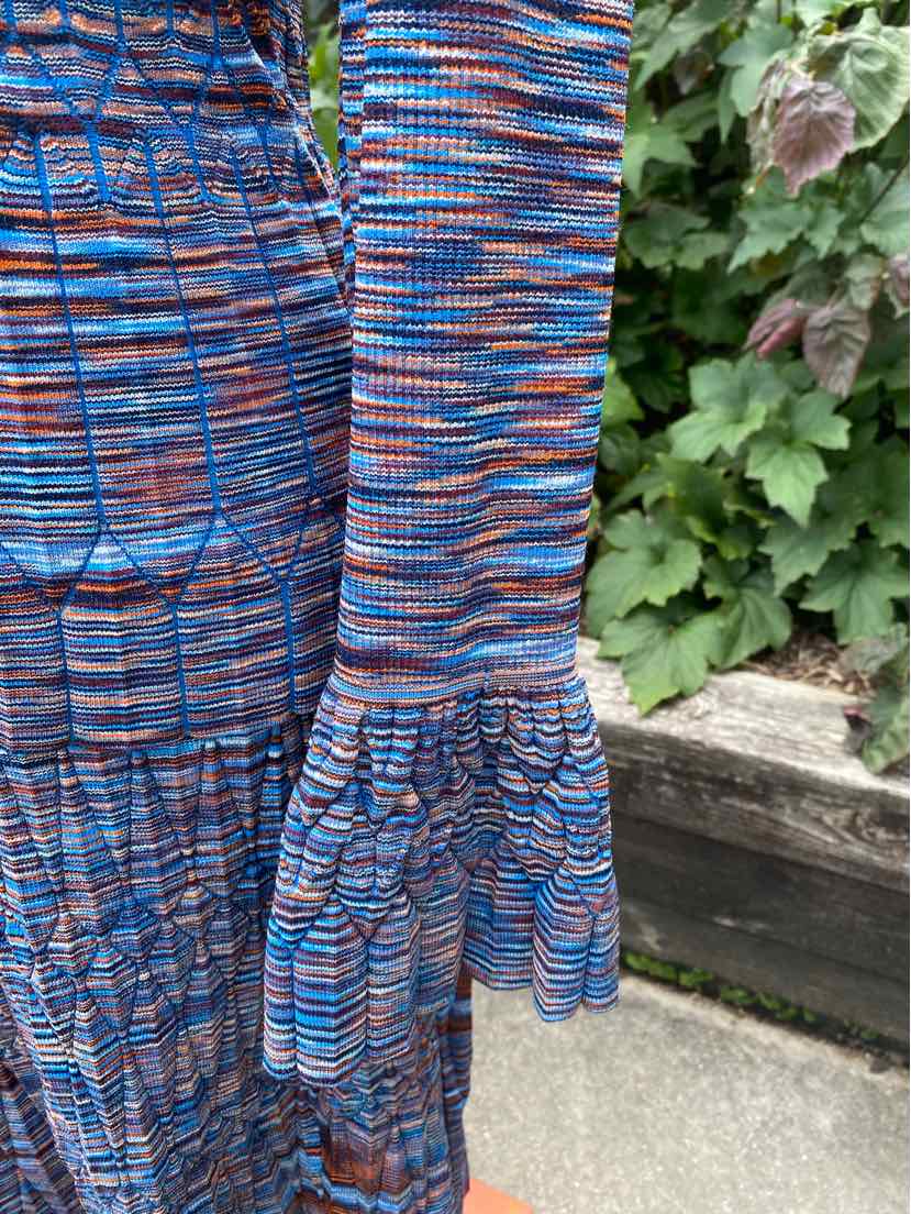 Long-sleeve top with blue, orange, and black space-dyed pattern and flared bell cuffs.