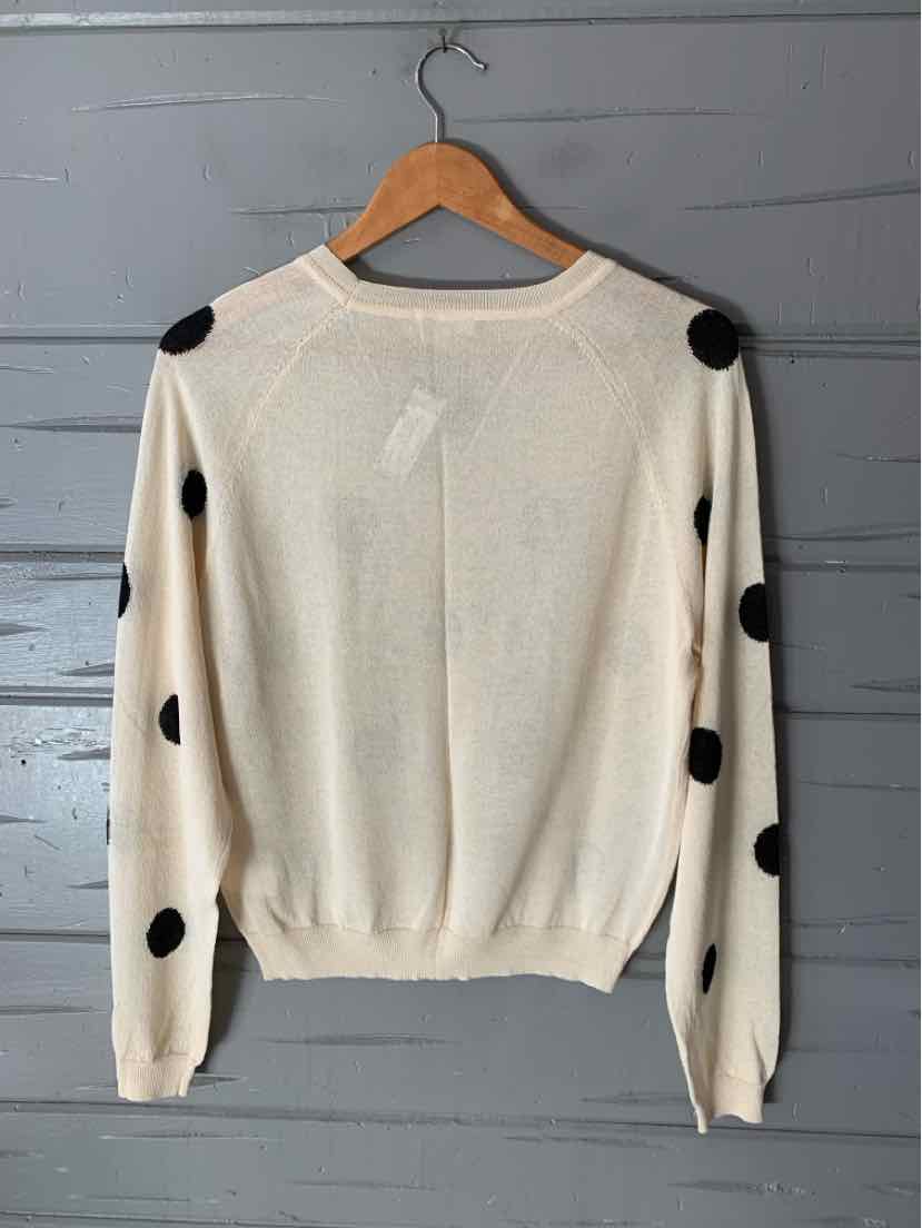 Cream knit sweater with large black polka dots, long sleeves, and a ribbed crew neck and hem.