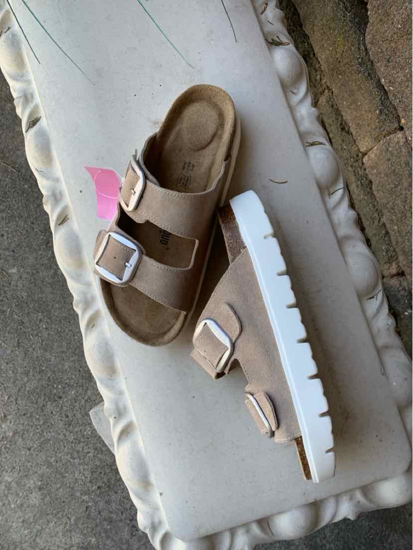 Sandal with light tan suede straps, two adjustable silver buckles, and thick white ridged sole, size 10.