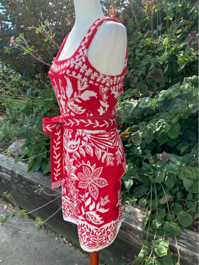 Red sleeveless dress with white paisley and floral print, tie belt, and scoop neckline.