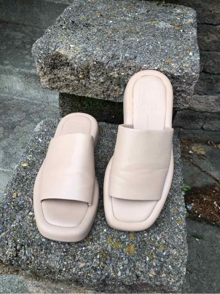 Nude slip-on sandals with wide strap and square toe on stone surface.