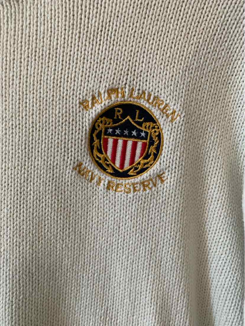 Cream knit fabric with embroidered Ralph Lauren crest in red, blue, gold, and white on chest.