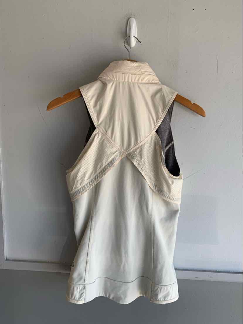 Light beige sleeveless athletic top with crisscross back straps hanging on wooden hanger.