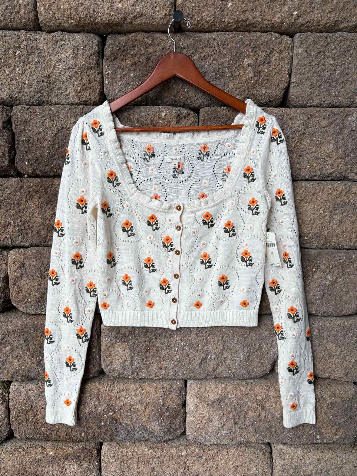 White cropped long-sleeve cardigan with orange and green floral print and a V-neckline.