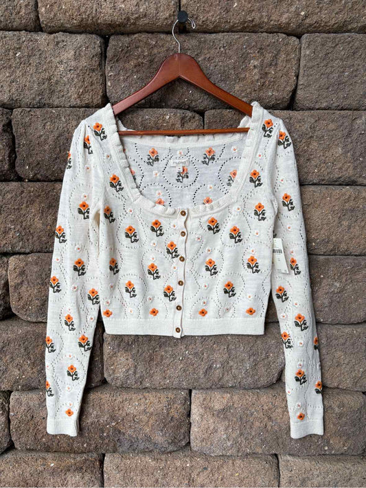 White cropped long-sleeve cardigan with orange and green floral print and a V-neckline.