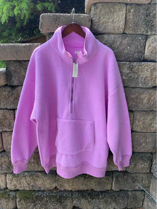 Lavender pullover with half-zip and front kangaroo pocket hanging on wooden hanger against stone wall.