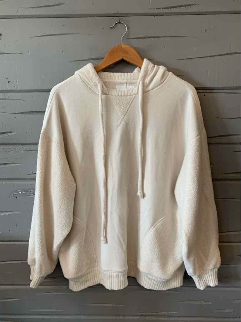Cream-colored oversized hoodie with front kangaroo pocket and drawstring hood hanging on wooden hanger.