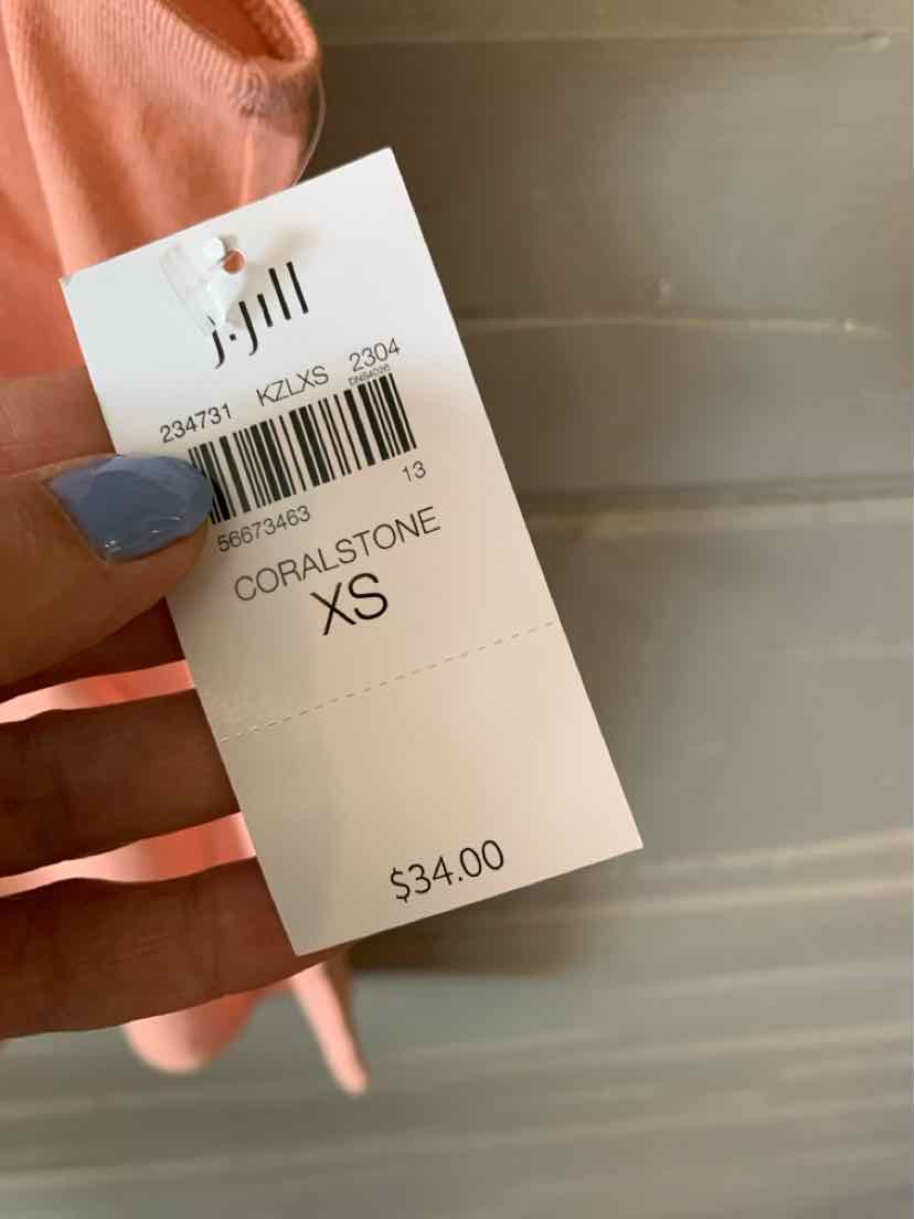 White clothing tag showing brand JJill, color Coralstone, size XS, and price $34, held against a background with a.