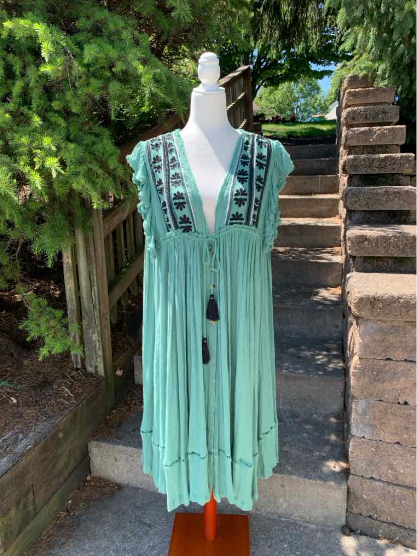 Light teal sleeveless dress with deep V-neck, black floral embroidery, and tassel ties on mannequin outdoors.