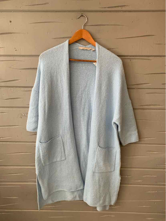 Light blue open-front cardigan with three-quarter sleeves and front pockets hanging on wooden hanger.