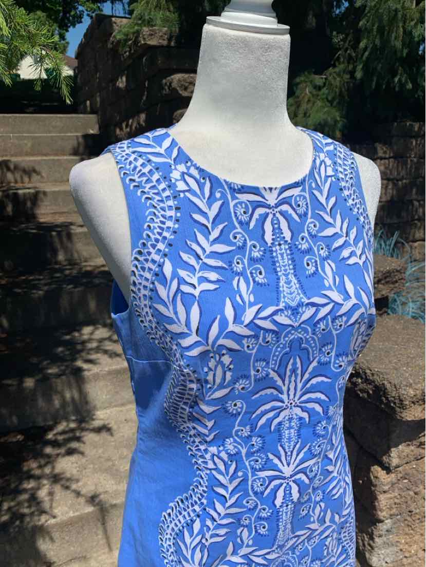 Sleeveless blue dress with white floral and leaf pattern, fitted waist, scoop neckline.
