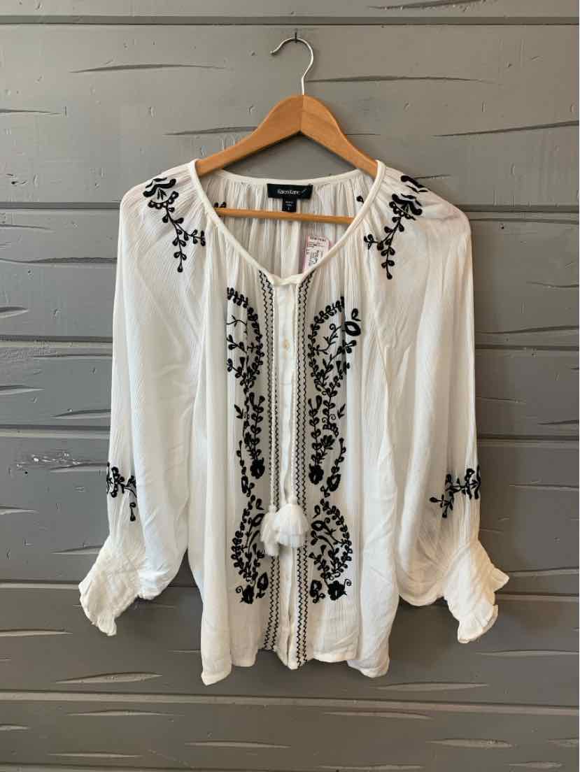 White long-sleeve blouse with black floral embroidery and tassel tie neckline.