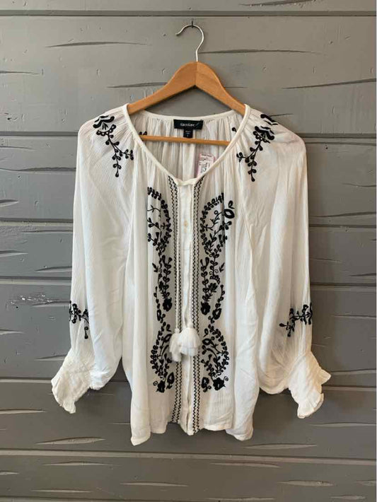 White long-sleeve blouse with black floral embroidery and tassel tie neckline.