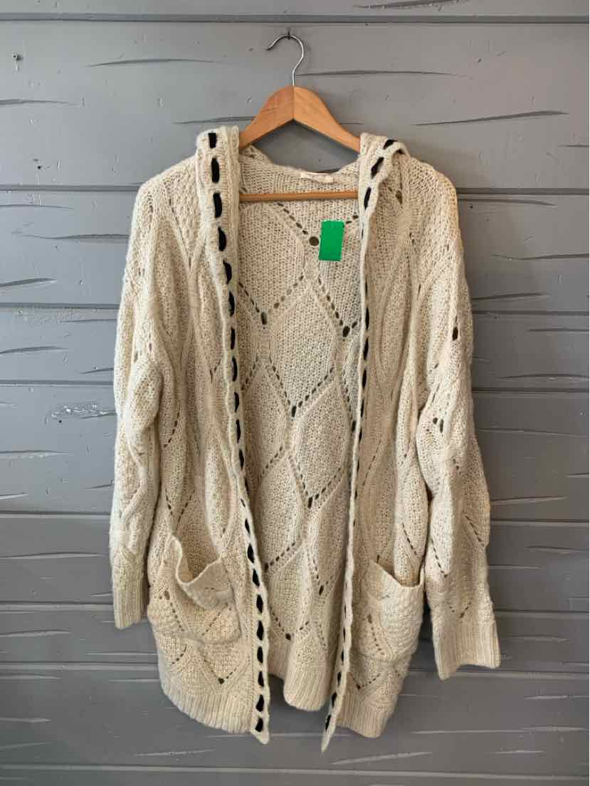 Cream-colored chunky knit cardigan with hood, cable knit pattern, front pockets, and button accents on sleeves.