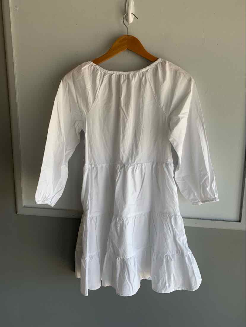 White long-sleeve tiered dress with gathered waist and round neckline on wooden hanger.