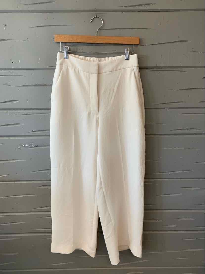 Cream high-waisted wide-leg trousers with front zipper and belt loops, hanging on wooden hanger.
