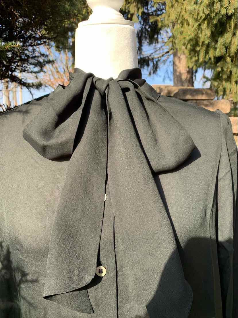 Black blouse with long sleeves and large tied bow collar on mannequin.