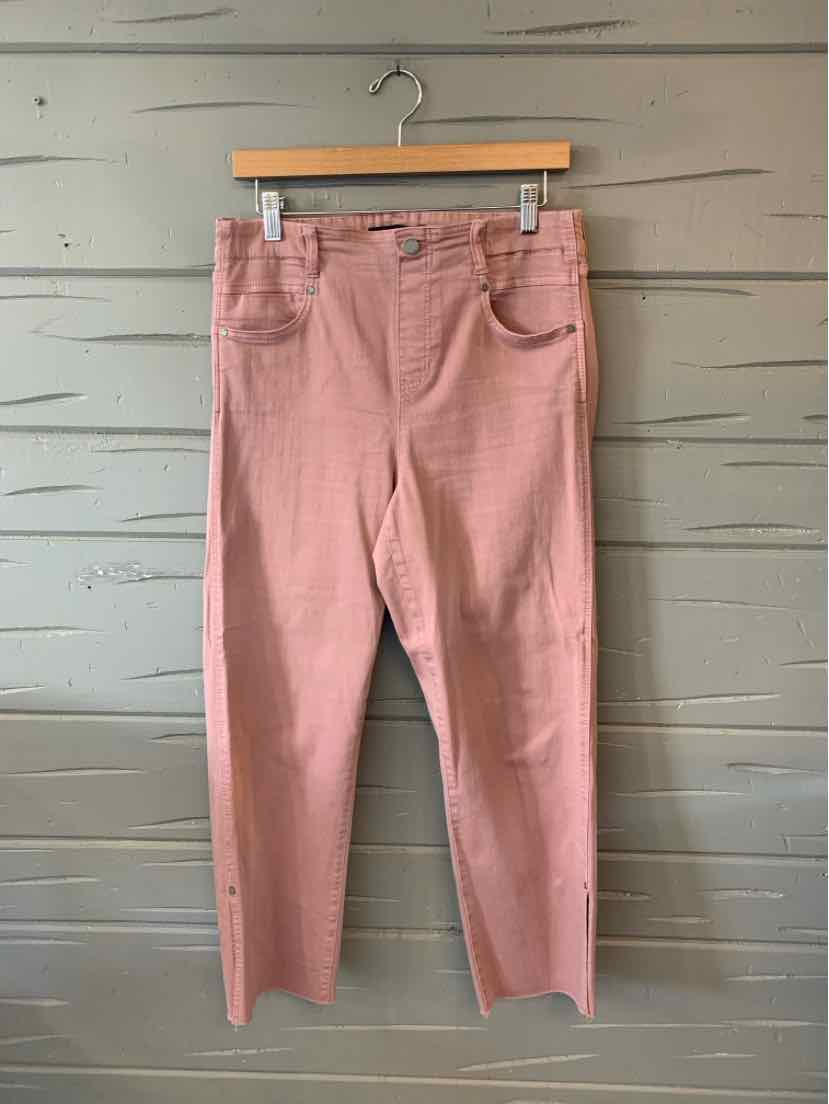 Light pink straight-leg pants with front pockets and belt loops hanging on wooden hanger against gray wood panel wall.