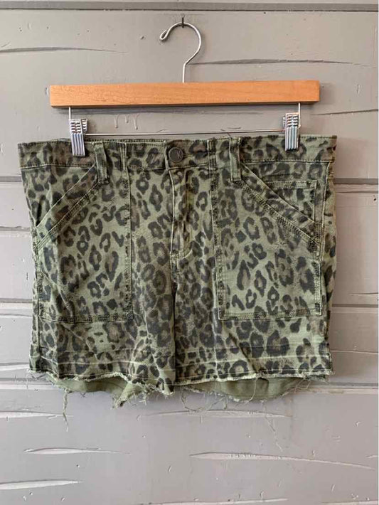 Green leopard print shorts with frayed hem hanging on wooden hanger.